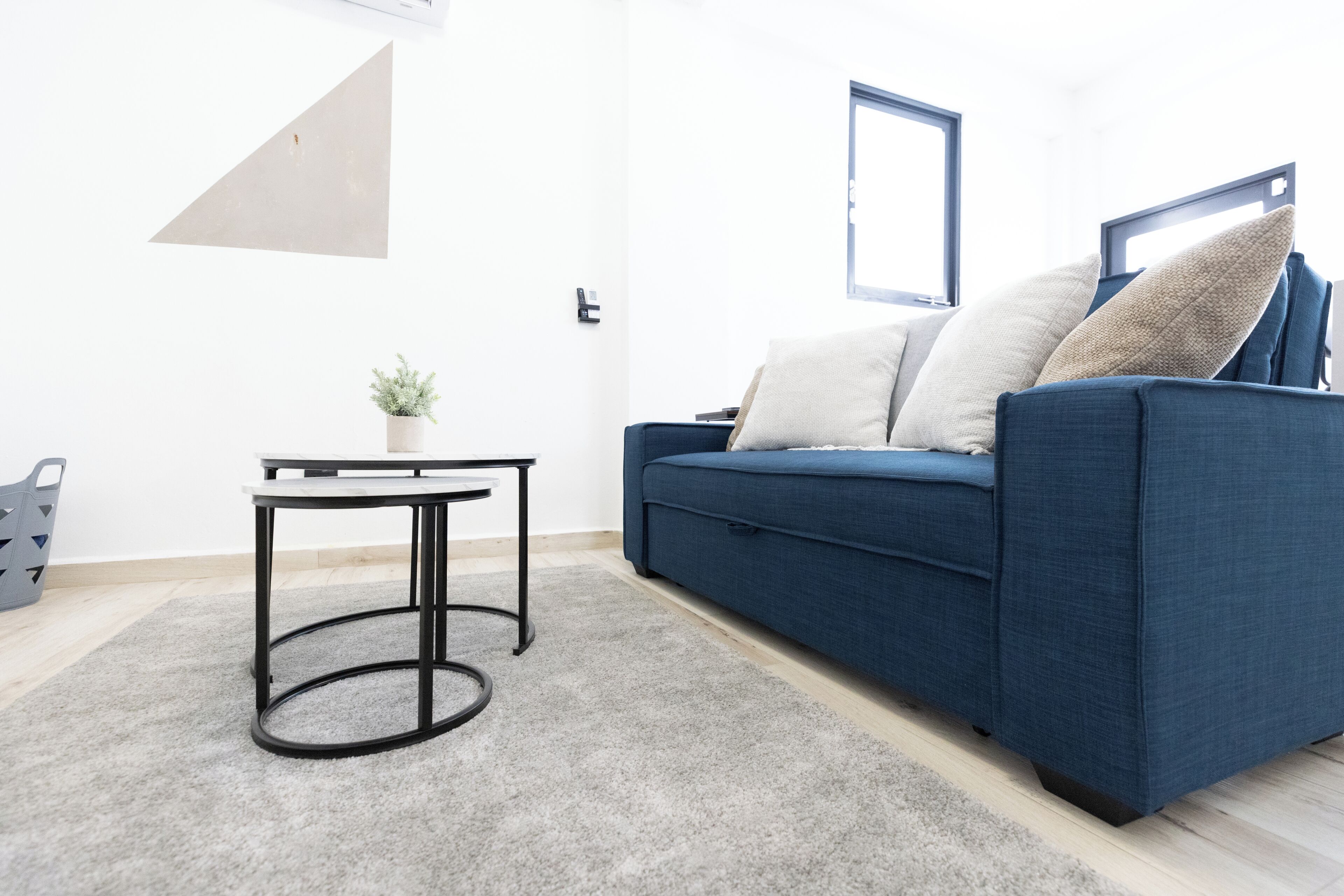 Una sala de estar moderna con un sofá azul, una pequeña mesa redonda y una planta en maceta.