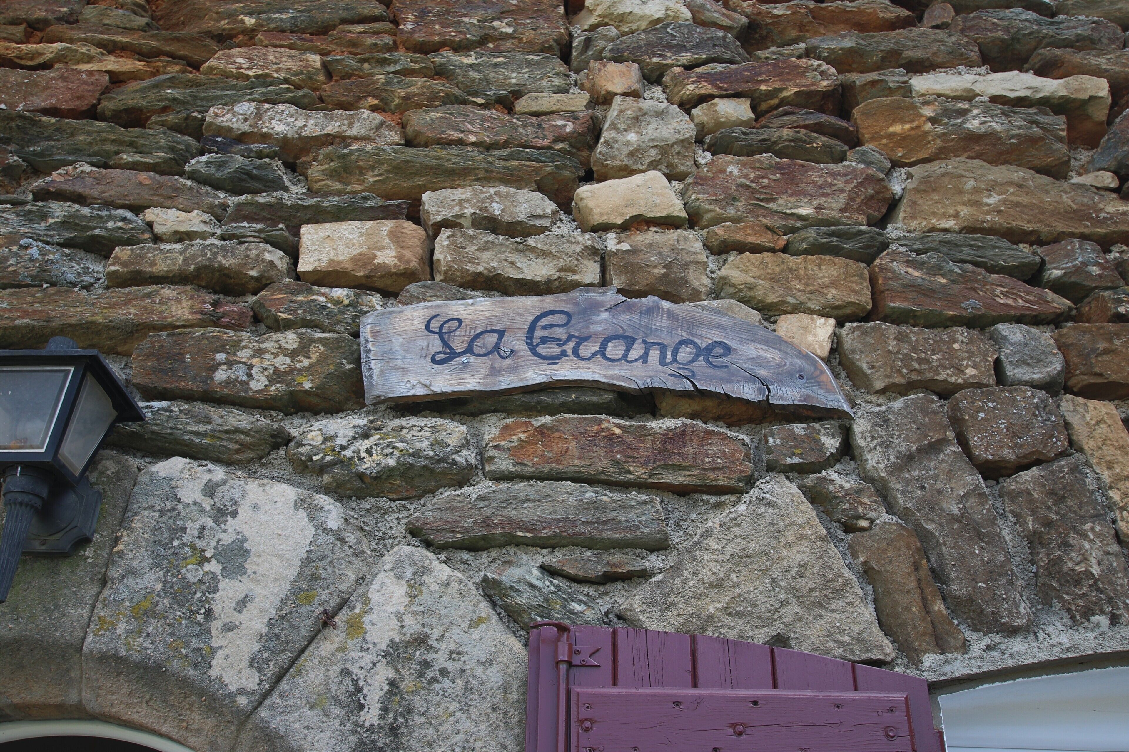 Un muro di pietra con un cartello che riporta 'La Erance' e una porta viola.