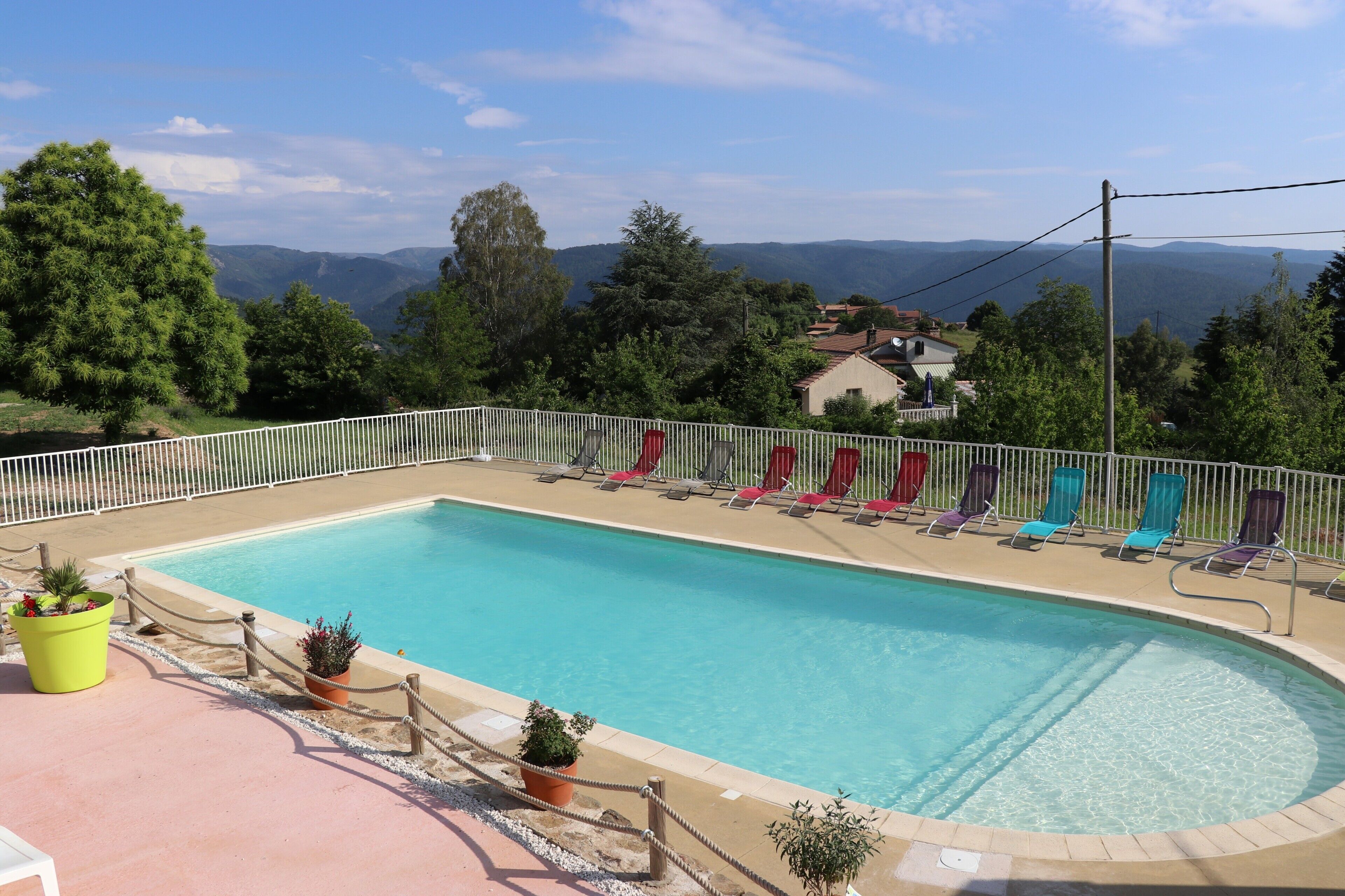 Une piscine avec vue sur les montagnes, entourée de chaises longues et de plantes en pot.