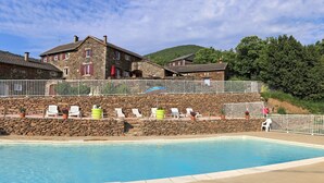 Un edificio de piedra con piscina, sillas blancas y valla blanca.