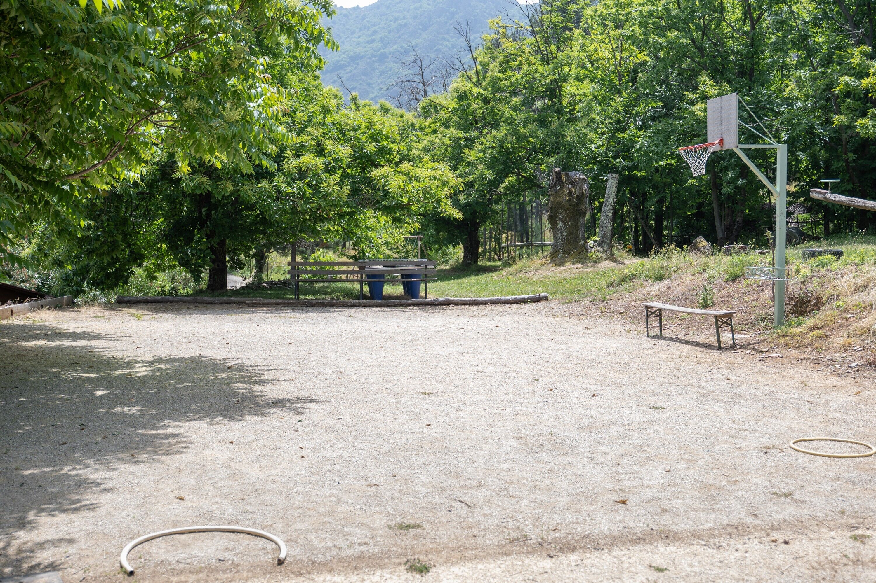 Ein Basketballplatz im Freien mit Bank, Bäumen und einem Bergpanorama.