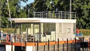Un'imbarcazione moderna con cabina in vetro, ponte in legno e ringhiera in metallo.