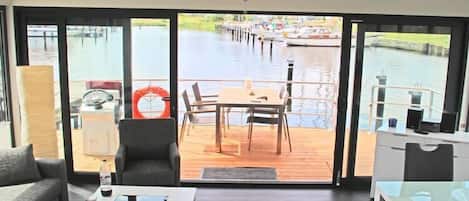 Een modern interieur met een grote schuifglazen deur die uitkomt op een terras met uitzicht op een waterweg.