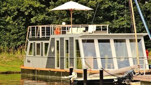 A houseboat docked at a pier with a covered deck area and a small cabin. - Hausboot in Ueckermuende (Ueckermünde)