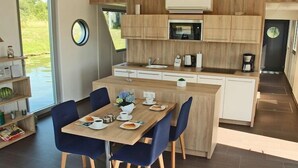 A modern kitchen with wooden cabinetry, a central island, and a dining area with blue chairs. - Hausboot in Ueckermuende (Ueckermünde)