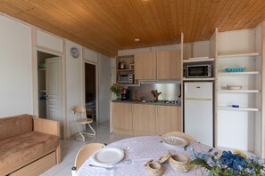 Cocina compacta con armarios de madera, microondas, refrigerador y comedor con una mesa para dos.