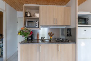 Una cocina compacta con armarios de madera, un microondas integrado, una estufa a gas y un lavamanos.