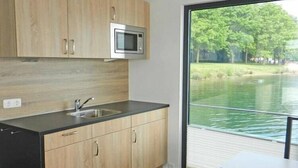 Une cuisine moderne avec des meubles en bois, un four à micro-ondes en acier inoxydable et une grande fenêtre donnant sur un plan d’eau.