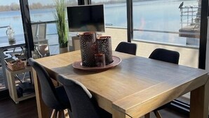 A modern dining area with a wooden table and chairs, large windows offering a view of a lake, and a decorative vase on the table.