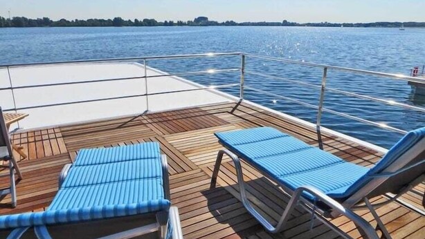 A deck with lounge chairs and a table, overlooking a calm body of water.