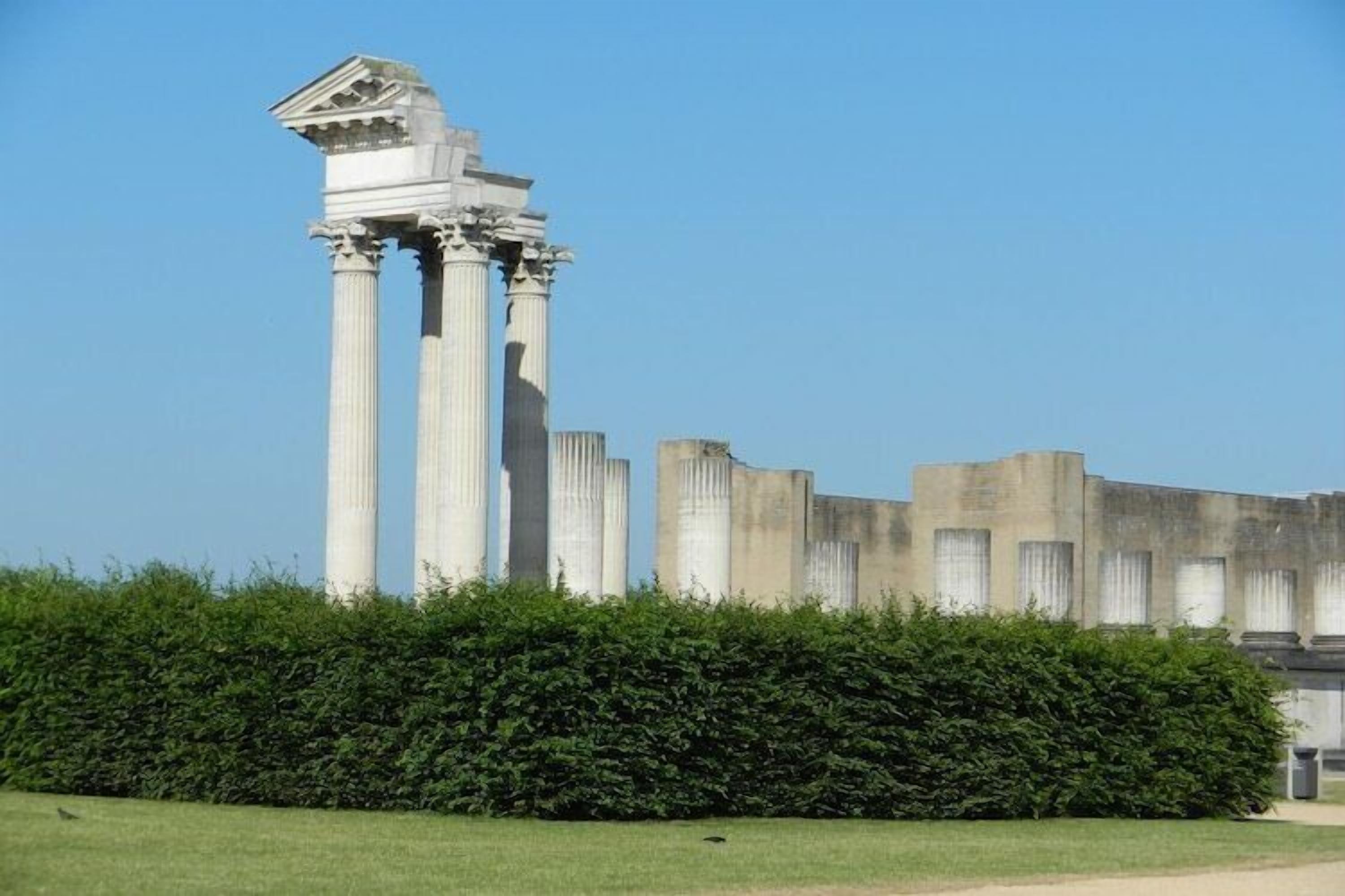Ancient columns with a classical structure, surrounded by a well-maintained hedge.
