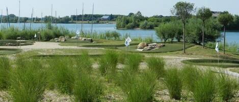 Un campo de golf con un lago al fondo, rodeado de árboles y zonas verdes.