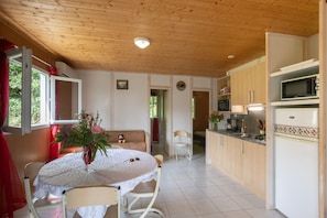 Een kleine keuken met een eethoek, houten plafond en uitzicht door een open deur.