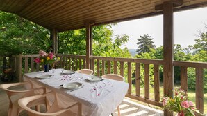 Eine hölzerne Terrasse im Freien mit Esstisch und Stühlen, mit Blick auf eine üppige grüne Landschaft.