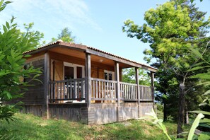 A wooden cabin with a porch, surrounded by trees.