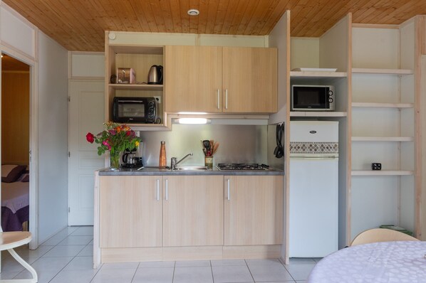 A compact kitchen with wooden cabinets, a microwave, a stove, and a refrigerator.