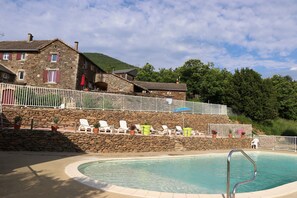 Um edifício de pedra com piscina, cadeiras brancas e cerca branca.