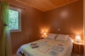 Um quarto com painéis de madeira, uma cama, duas luminárias de cabeceira, uma janela com cortina e uma pequena mesa de cabeceira com abajur.