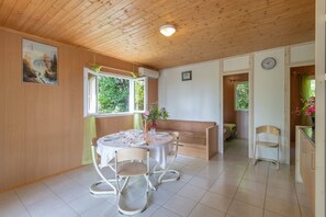 Uma sala de jantar com uma mesa redonda, cadeiras, um banco e uma janela com vista para o verde.