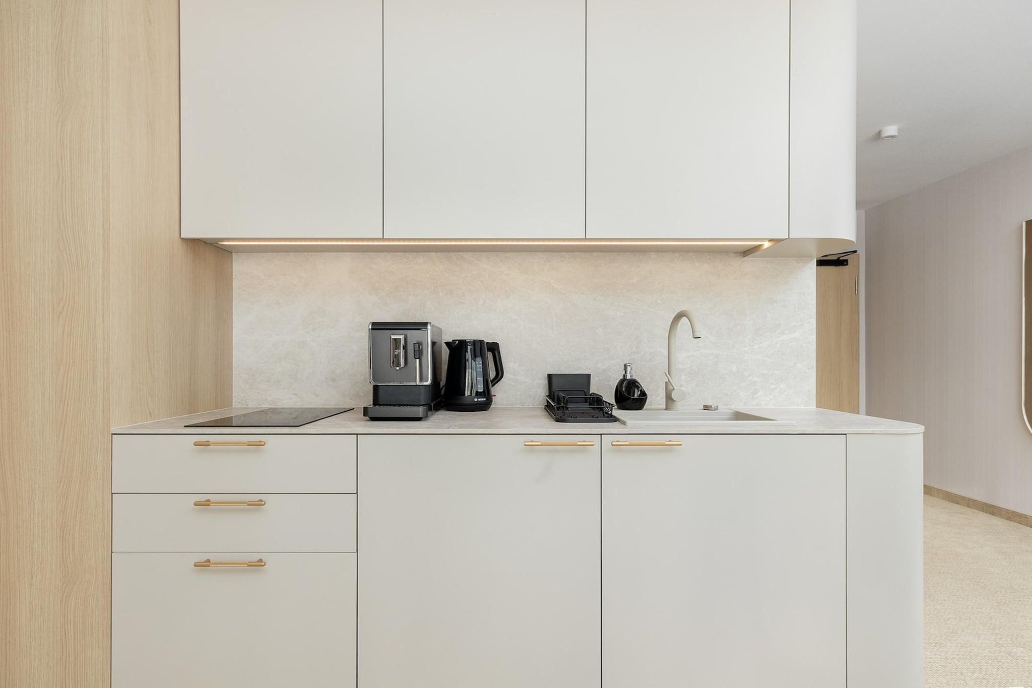 A modern kitchen with a built-in coffee maker, a kettle, and a sink.