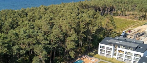 A residential area with a swimming pool, modern buildings, and a dense forest.