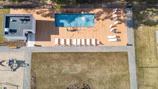An aerial view of a property with a swimming pool, sun loungers, a small building, and a fenced area with a playground.