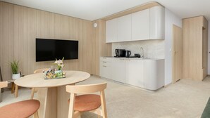 A modern kitchen with white cabinets, a flat-screen TV mounted on the wall, and a dining area with a round table and chairs.