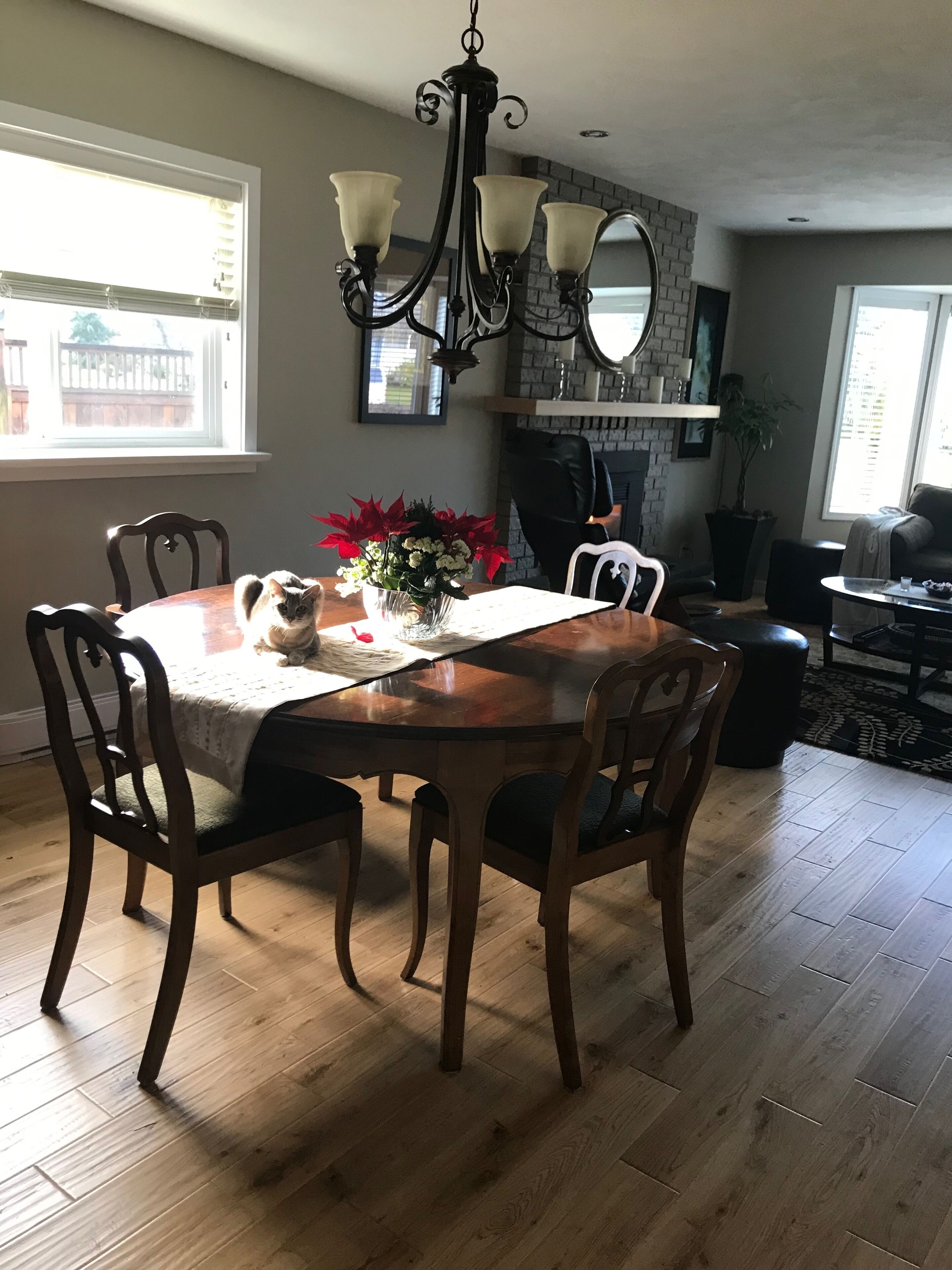 A dining room with a wooden table, four chairs, a chandelier, and a vase with flowers.