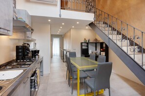 Une cuisine moderne équipée d’une cuisinière à gaz, un coin repas avec une table et des chaises en verre, et un escalier agrémenté de rampes décoratives.