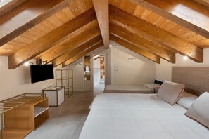 Une chambre avec un plafond en pente, un lit, une télévision et un bureau.