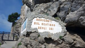 Ein Schild an einer felsigen Klippe mit dem Text 'BENVENUTI SUL SENTIERO DEGLI DEI'.