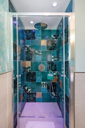A shower with a glass enclosure, a handheld showerhead, and a wall with a mosaic tile pattern.