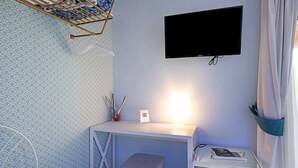 Ein Zimmer mit Schreibtisch, Stuhl, Wandfernseher und einem kleinen Nachttisch.