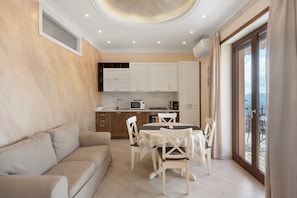 A modern kitchen with white cabinets, a dining table with chairs, and a balcony with a view.