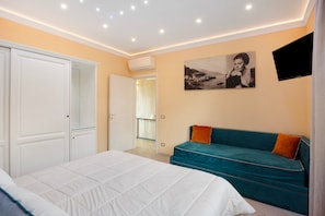 A bedroom with a bed, a teal sofa, a TV, and a painting on the wall.