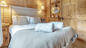 A wooden cabin bedroom with a large bed, two bedside lamps, a dresser, and a mirror on the wall. - 1 bedroom accommodation in Hexham (Hexham)