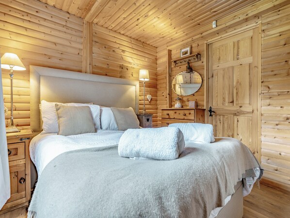 Une chambre à coucher dans un chalet en bois, avec un grand lit, deux lampes de chevet, une commode et un miroir au mur.
