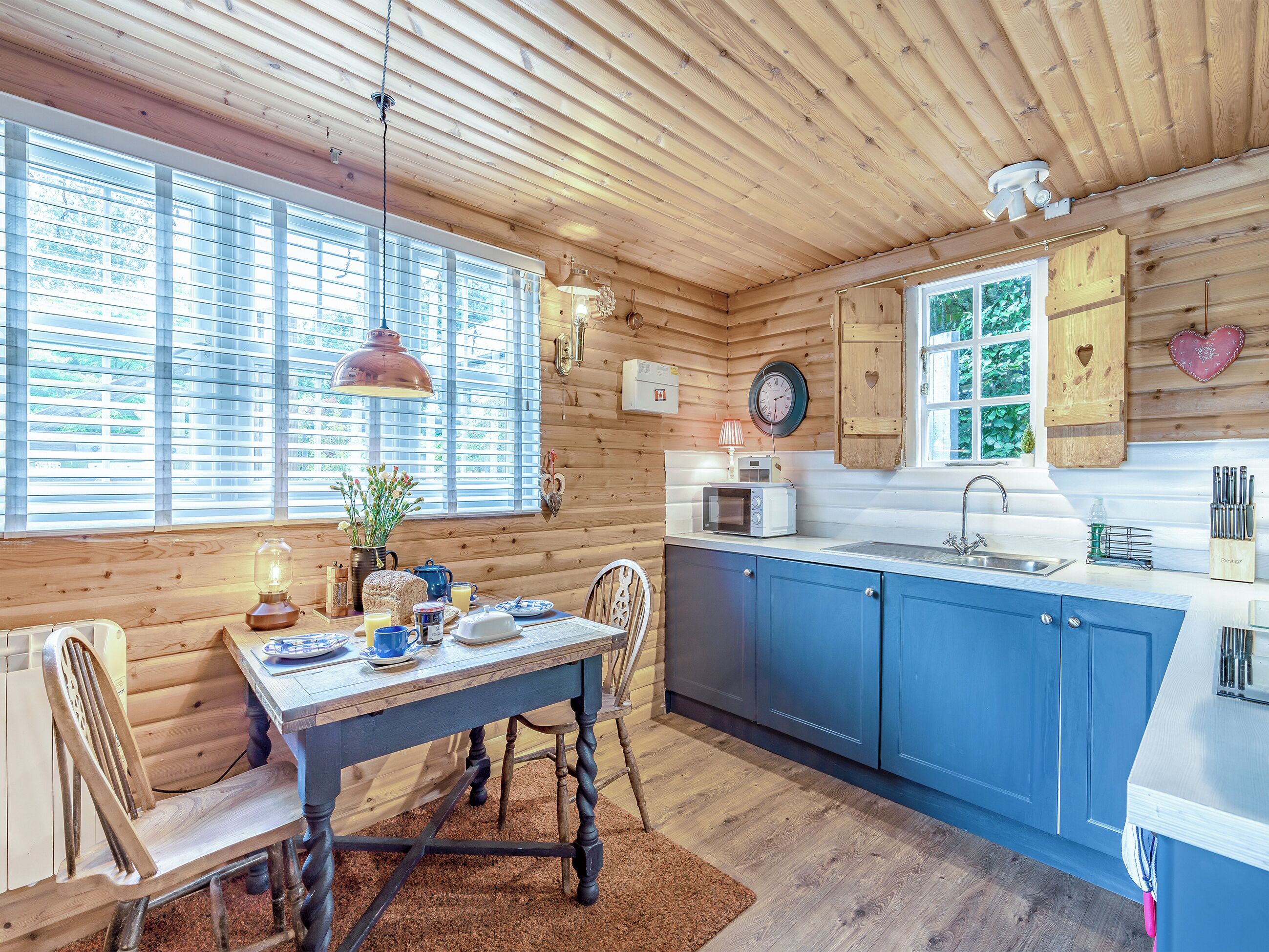 A cozy cabin-style kitchen with wooden walls, a dining table with chairs, a sink, and a clock on the wall.