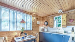 A cozy cabin-style kitchen with wooden walls, a dining table with chairs, a sink, and a clock on the wall. - 1 bedroom accommodation in Hexham (Hexham)