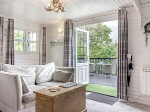 Une pièce chaleureuse avec un canapé blanc, une table basse en bois et une vue sur un balcon doté d’une balustrade.
