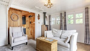 A cozy living room with a white sofa, a white armchair, and a wooden coffee table. There is a fireplace, a wooden door, and a window with curtains. - 1 bedroom accommodation in Hexham (Hexham)