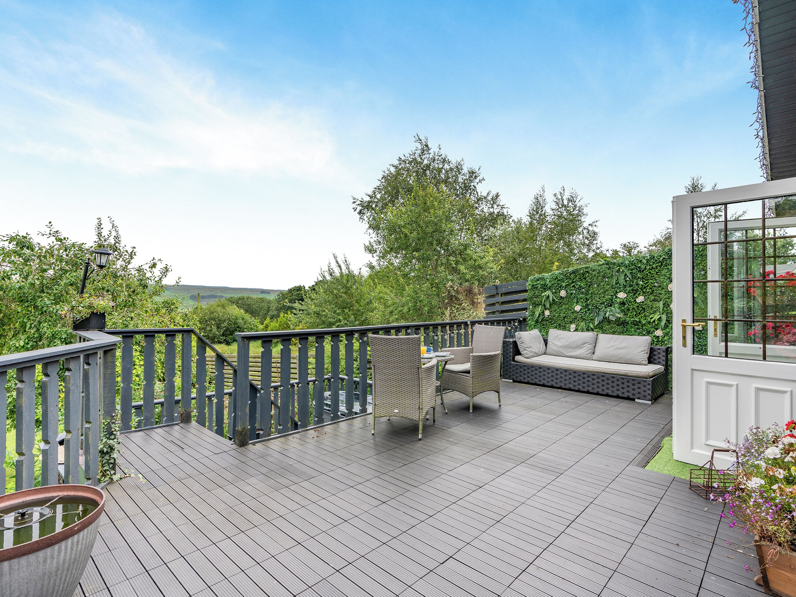 A deck with outdoor furniture, a potted plant, and a view of the surrounding greenery.