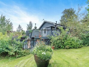 A wooden house with a porch, surrounded by lush greenery and a well-maintained lawn.