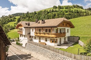 Une maison à deux étages avec un balcon, un mur en pierre et une cour gazonnée.