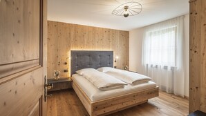 A wooden-paneled bedroom with a bed, bedside tables, and a window with curtains. - Apartment 'Désirée - Fanes' with Mountain View, Balcony and Wi-Fi (St. Vigil)