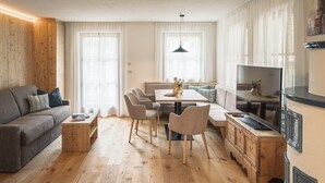 A modern living room with a sofa, dining table, chairs, and a TV. - Apartment 'Désirée - Fanes' with Mountain View, Balcony and Wi-Fi (St. Vigil)