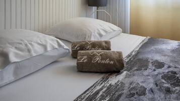 A bed with white linens, two brown towels with 'Le Ponton' text, a lamp, and a striped wall.