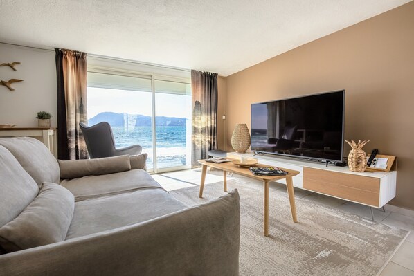 Una sala moderna con televisor grande, sofá, mesa de centro y vista al mar.