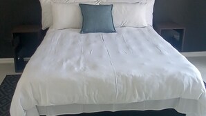 A bed with white bedding and a single blue pillow, a dark headboard, and a small bedside table. - 3-bedroom apartment in charming Walvis Bay with AC, WiFi (Walvis Bay)