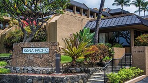 Un edificio con un letrero que dice "KONA PACIFIC" y un muro de piedra con un buzón.